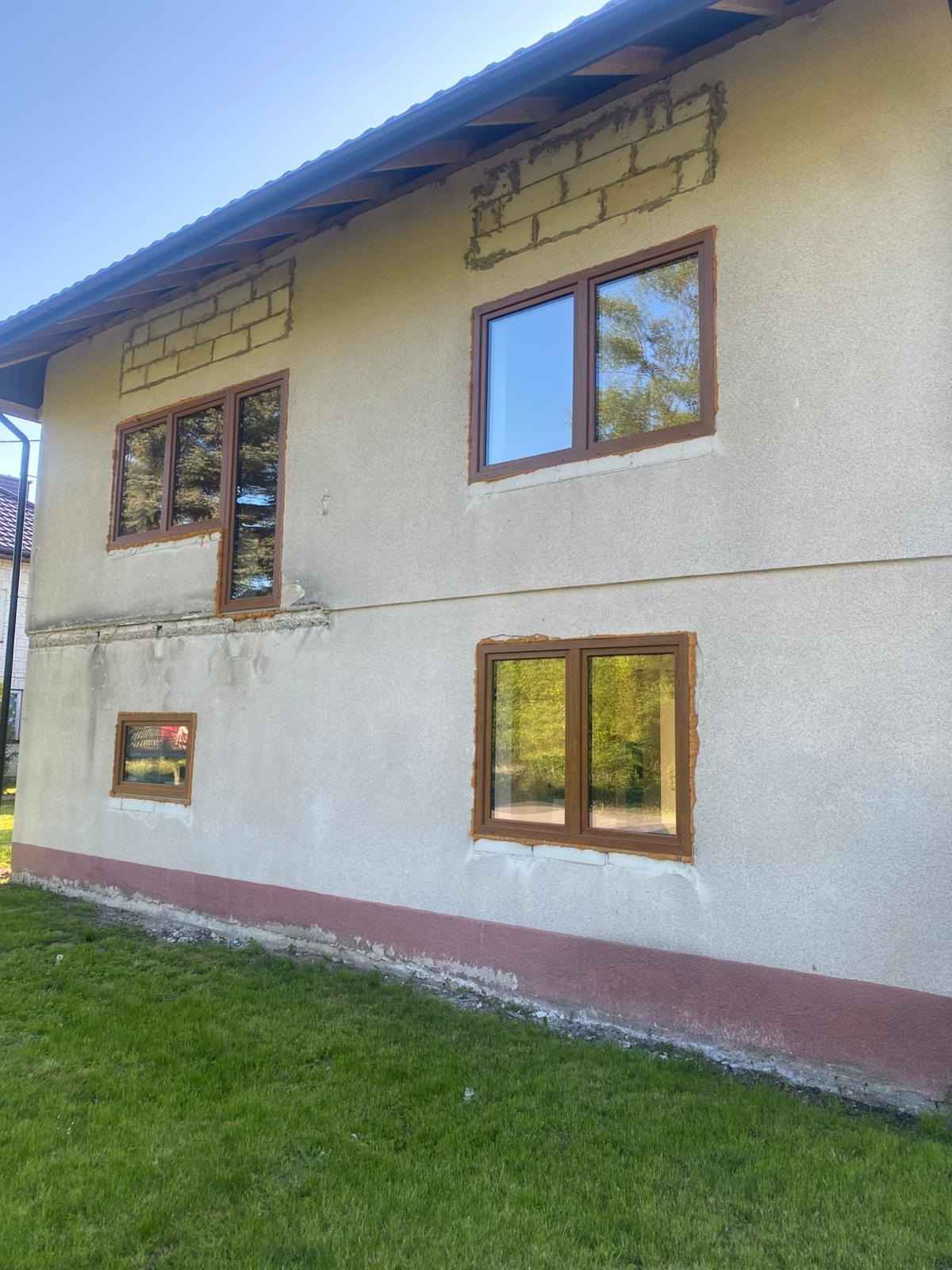 Stary dom z tynkiem typu baranek, odsłoniętymi nadprożami i bordowym cokołem